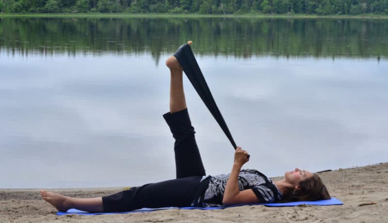 Femme faisant des étirements avec une bande élastique sur le bord d'un lac